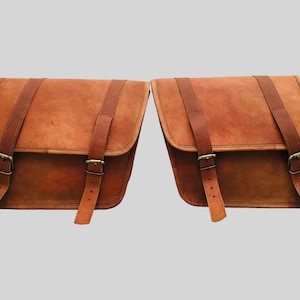 Könnte beinhalten: Zwei braune Leder-Motorradsatteltaschen mit Schnallen und Riemen.
