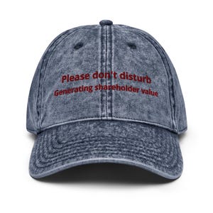 Puede incluir: Gorra de béisbol de mezclilla azul descolorido. El texto "Please don't disturb Generating shareholder value" está bordado en rojo. La gorra tiene una visera curva y un diseño clásico de seis paneles.