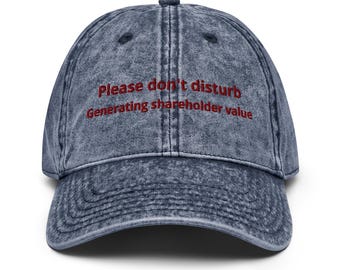 May include: A denim-style baseball cap in a faded blue hue. The cap features the embroidered text "Please don't disturb Generating shareholder value" in red. The hat has a curved brim and a classic six-panel design.