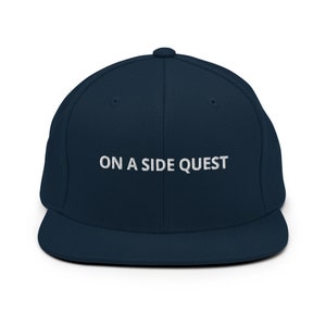 May include: A navy blue baseball cap with a white embroidered phrase "ON A SIDE QUEST".
