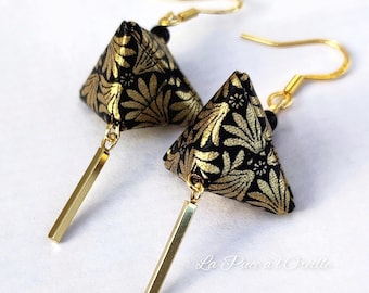 May include: A pair of gold earrings with black and gold patterned pyramid-shaped charms and gold dangle accents. The earrings are labeled "La Pucce et Stella".