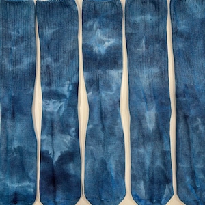 May include: Five pairs of knee-high socks with a tie-dye pattern in shades of blue. The socks are made of a ribbed knit fabric. The tie-dye effect creates a marbled appearance.