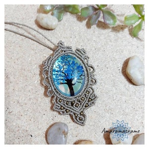 May include: A macrame necklace with a blue and green tree pendant. The pendant is made of a clear resin with a blue tree inside. The necklace is made of brown cord and has a brown cord tassel.
