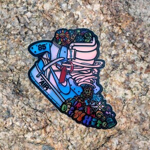 May include: A blue and pink Nike Air Jordan 1 shoe with a white swoosh and the text "AIR" and "OFF-WHITE" on the side. The shoe is decorated with flowers, peace signs, and other graphic elements.