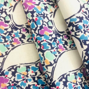 Peut inclure: Un tissu présentant un motif répétitif de contours bleu marine foncé formant des formes semi-circulaires. Le design est rempli de petites taches abstraites rappelant des fleurs dans des tons vifs de bleu, violet, vert menthe, jaune et rouge.