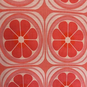 May include: A woven fabric featuring a repeating geometric pattern of stylised orange and pink flowers. Each flower is centred within a square frame with rounded corners, composed of concentric lines in shades of coral, peach, and cream.