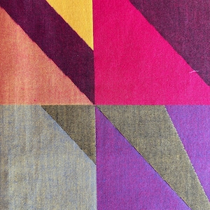 May include: Close-up of a geometric textile pattern. The design features large, angled shapes in vibrant colors, including yellow, orange, pink, purple, and gray. The fabric has a textured appearance, with visible woven threads.