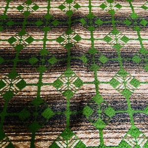 Peut inclure: Gros plan sur un tissu à motifs avec un motif répétitif. Le motif présente des lignes verticales et des losanges verts, ainsi que des rayures horizontales marron et beige. Le tissu a un aspect texturé.