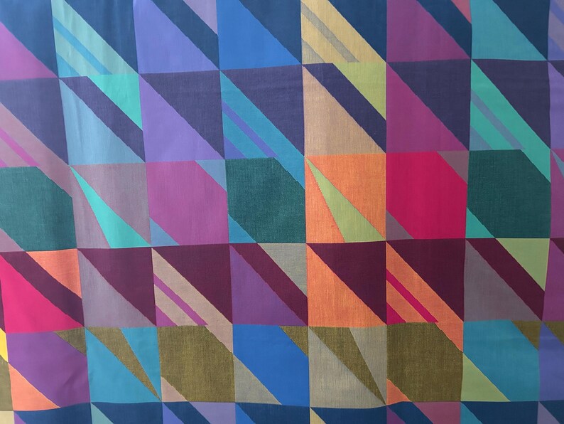 May include: A colorful textile with a geometric pattern. The design features squares and diagonal stripes in shades of blue, purple, green, orange, and pink. The fabric has a soft, slightly textured appearance.