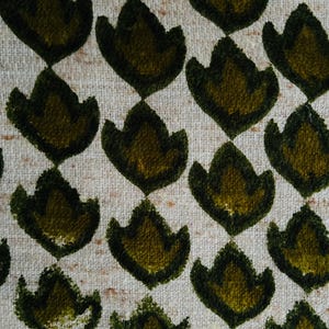 Op de afbeelding: Een close-up van een stof met een herhalend patroon van groene gestileerde bloemenvormen op een witte achtergrond.