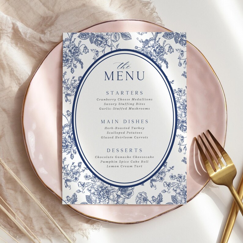 May include: A menu card with a floral design in blue and white, featuring an oval frame with the text "The Menu." The menu lists starters, main dishes, and desserts. The card is placed on a pink plate with a gold rim, accompanied by a gold fork.