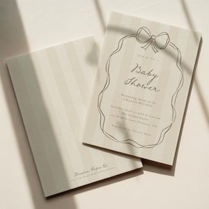 Può includere: Due inviti per baby shower con un motivo a righe color crema e beige. Un invito è aperto, mostrando il testo "Baby Shower" all'interno di una cornice decorativa. Il testo include il nome dell'invitato d'onore, la data, l'ora e il luogo.