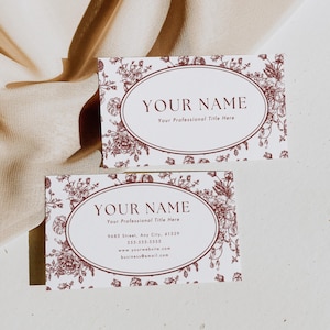 Puede incluir: Dos tarjetas de visita con un diseño floral en burdeos y blanco. Cada tarjeta tiene un marco ovalado con el texto "YOUR NAME" y "Your Professional Title Here". La tarjeta inferior incluye información de contacto.
