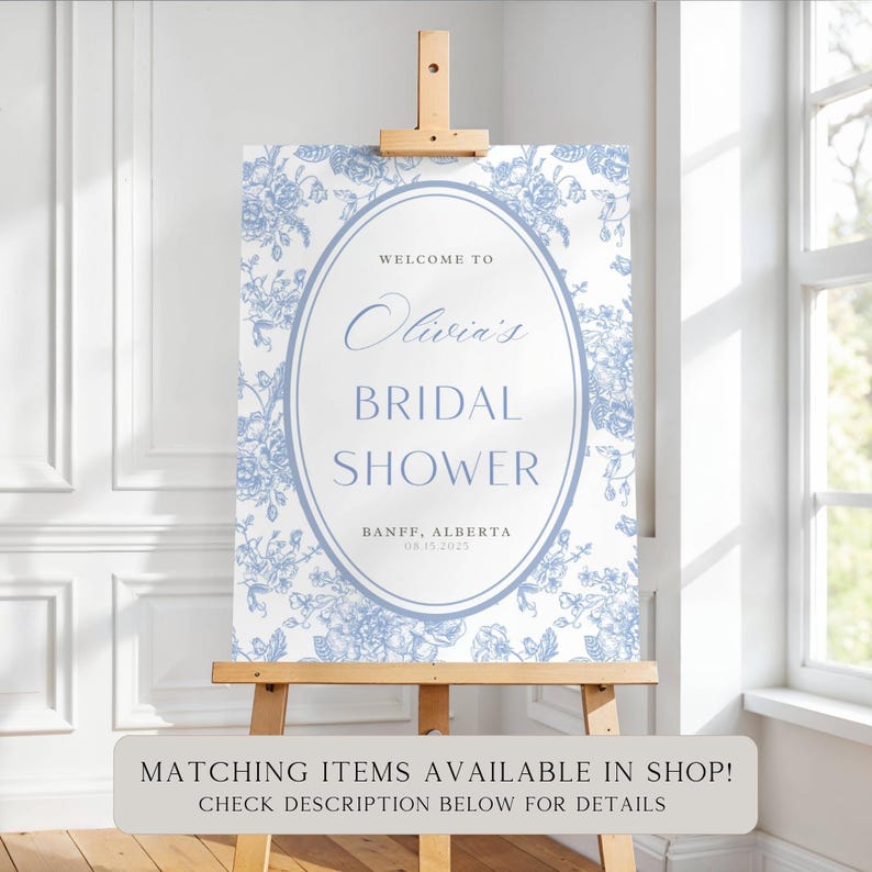 Pu&ograve; includere: Un cartello per l'addio al nubilato su un cavalletto di legno. Il cartello presenta un motivo floreale in blu chiaro e bianco, con il testo "Welcome to Olivia's Bridal Shower" e la data 15/08/2025. Banff, Alberta.