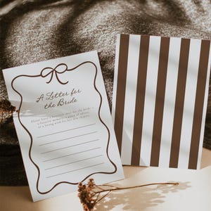 May include: A white card with the text "A Letter for the Bride" in brown script, featuring a decorative border and space for writing. A second card with brown and white vertical stripes is also visible.