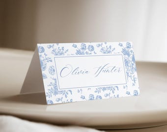 May include: A white place card with a blue floral pattern and the name "Olivia Hunter" printed in blue cursive script.
