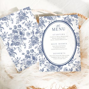 May include: Two white and blue floral patterned menu cards. The menu cards have a navy blue oval in the center with the word "MENU" at the top. The menu lists starters, main dishes, and desserts.