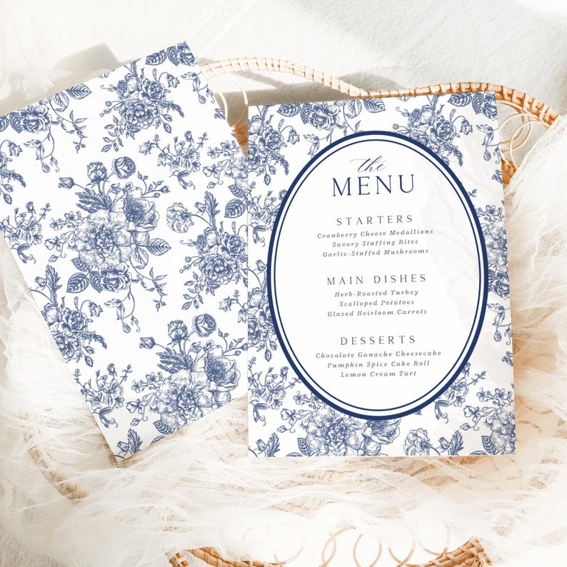 May include: Two white and blue floral patterned menu cards. The menu cards have a navy blue oval in the center with the word "MENU" at the top. The menu lists starters, main dishes, and desserts.
