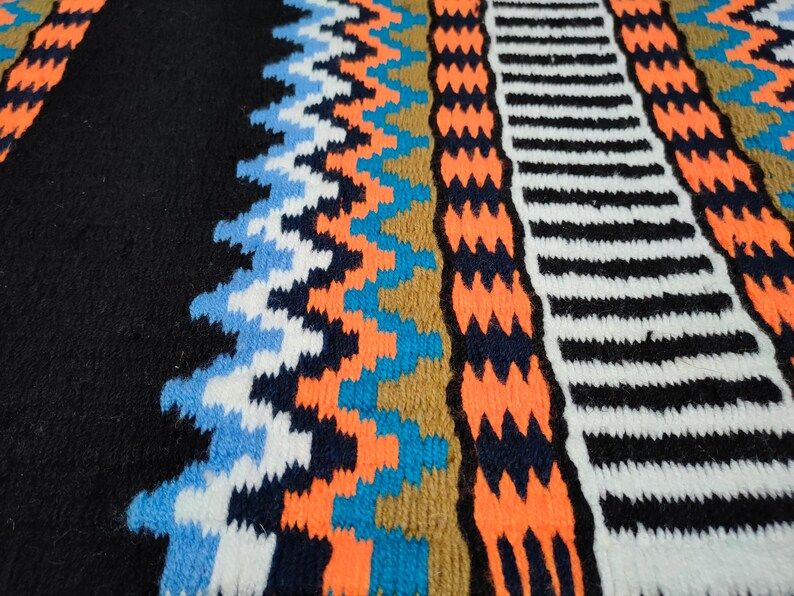 May include: Close-up of a colorful knitted fabric with geometric patterns in shades of blue, orange, white, and black.