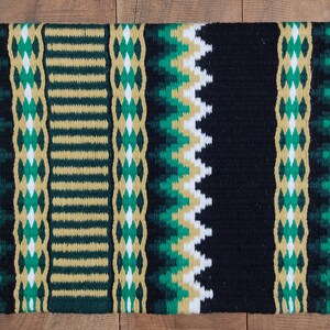 May include: A black, green, and gold woven saddle blanket with a geometric pattern.