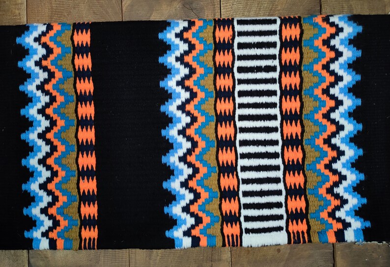 May include: A black saddle blanket with a colorful geometric pattern in shades of orange, blue, white, and brown. The pattern is woven into the fabric and creates a visually appealing design.
