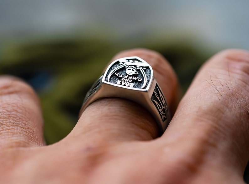 May include: A silver ring with a raised design featuring a skull and the text "БОЯР 1980 СМЕРТЬ". The ring is worn on a person's finger.