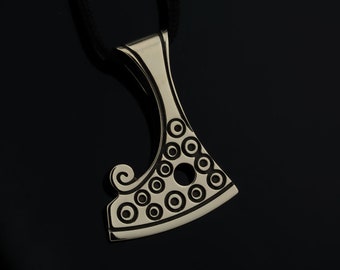 May include: A silver pendant in the shape of an axe with a circular pattern and a swirl design. The pendant is on a black cord.