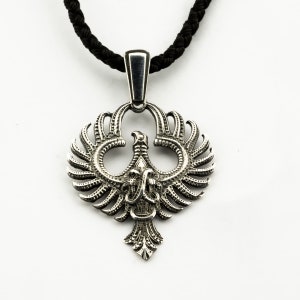 May include: A silver pendant necklace featuring a detailed design of a stylized bird with spread wings. The pendant is attached to a black cord.