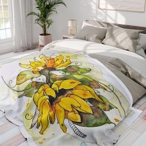 Peut inclure: Une couverture blanche avec une illustration à l'aquarelle d'un tournesol. Le tournesol a des pétales jaune vif, des feuilles vertes et un centre brun. La couverture est sur un lit avec une literie de couleur neutre.