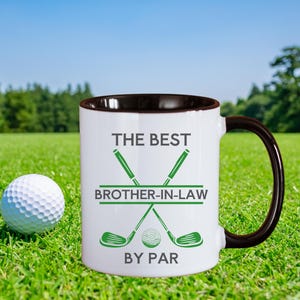 May include: White coffee mug with a brown interior and handle, featuring the text "THE BEST BROTHER-IN-LAW BY PAR" in green. The design includes crossed golf clubs and a golf ball. A golf ball sits on the green grass next to the mug.
