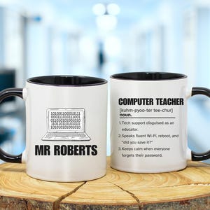 Puede incluir: Taza de cerámica blanca con asa e interior negros. Un lado presenta un gráfico de portátil con código binario y el nombre "MR ROBERTS". El otro lado tiene la definición de "PROFESOR DE INFORMÁTICA".