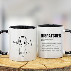 Puede incluir: Taza de cerámica blanca con interior y asa negros. Un lado presenta un gráfico de auriculares con una línea de latidos y el nombre "Taylor". El otro lado tiene la definición de "DISPATCHER".