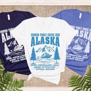 以下が含まれることがあります： 旅行をテーマにしたデザインのTシャツ3枚。シャツはネイビーブルー、白、青です。各シャツには、大きな青い文字で「ALASKA」という単語と、山とクルーズ船のグラフィックが描かれています。「JOHNSON FAMILY CRUISE」と年号のテキストも含まれています。
