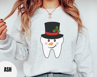 May include: A grey sweatshirt featuring a white tooth wearing a black top hat with a red band and green holly. The tooth has a carrot nose and rosy cheeks.