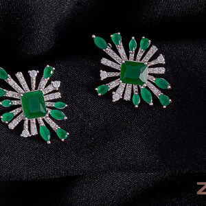 May include: A pair of silver earrings with green square gemstones and smaller clear gemstones. The earrings have a starburst design.