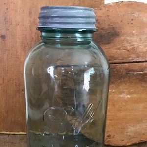 May include: A vintage, teal-colored Ball Perfect Mason jar with a metal lid. The jar has embossed lettering and a classic design, perfect for canning or rustic decor. The jar is approximately 6 inches tall.