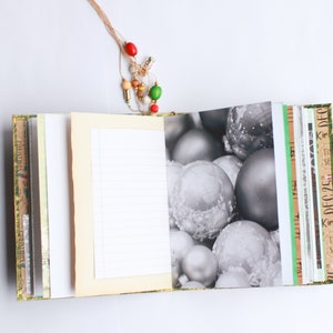 May include: A blank journal with a cream-colored cover and a decorative paper spine. The journal is open to a blank page with lined paper. The other side of the journal has a black and white photo of silver Christmas ornaments.