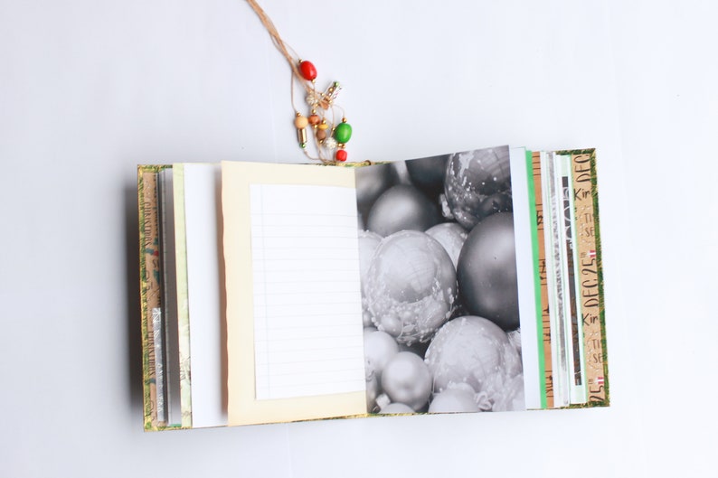 May include: A blank journal with a cream-colored cover and a decorative paper spine. The journal is open to a blank page with lined paper. The other side of the journal has a black and white photo of silver Christmas ornaments.