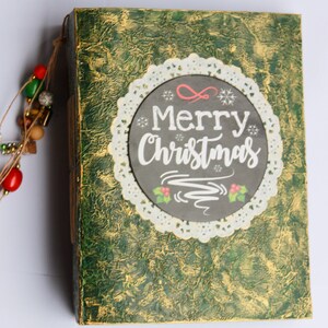 May include: A green and gold journal with a white lace doily and a black chalkboard circle that says "Merry Christmas".