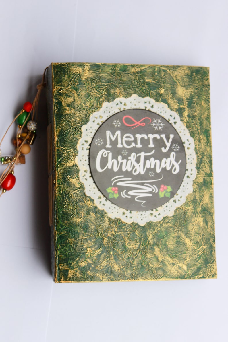 May include: A green and gold journal with a white lace doily and a black chalkboard circle that says "Merry Christmas".