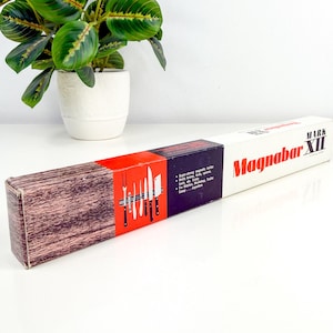 Puede incluir: Una caja rectangular para un soporte de cuchillos Magnabar XII. La caja es blanca, roja, negra y marrón. La caja tiene las palabras "Magnabar XII" impresas. La caja tiene una ilustración de cuchillos en una tira magnética.