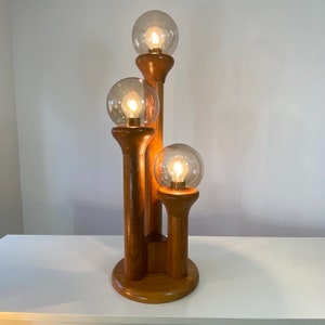 May include: A wooden table lamp with three glass globes. The lamp has a mid-century modern design and is made of natural wood.