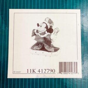 Op de afbeelding: Een beeldje van Mickey Mouse als koning, met kroon en scepter. De afbeelding bevat de tekst "11K 412790" en een Disney copyright-vermelding, tegen een witte achtergrond.