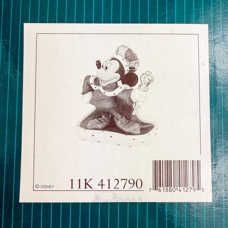 Op de afbeelding: Een beeldje van Mickey Mouse als koning, met kroon en scepter. De afbeelding bevat de tekst "11K 412790" en een Disney copyright-vermelding, tegen een witte achtergrond.