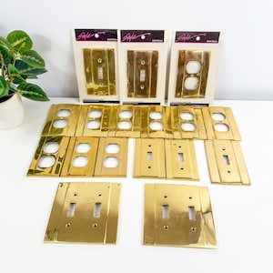 May include: A collection of gold brass electrical outlet and switch covers. Some are still in their original packaging, labeled "Style" and "Solid Brass." The covers are in various configurations, including single and double switch plates and outlet covers.