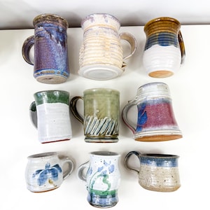 Puede incluir: Colección de nueve tazas de cerámica hechas a mano en varios colores y patrones. Las tazas presentan una variedad de diseños, que incluyen rayas, remolinos y motivos florales.