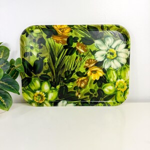 May include: Rectangular serving tray with a vibrant floral pattern. The tray features a glossy finish and a design of yellow, white, and green flowers with dark green foliage against a light green background. The tray is on a white surface.