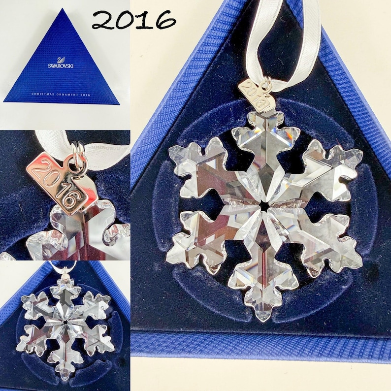 May include: A clear faceted crystal snowflake ornament with a silver-tone metal tag engraved with the year 2016. The ornament hangs from a white ribbon and is presented in a triangular blue box with the Swarovski logo and text 2016.