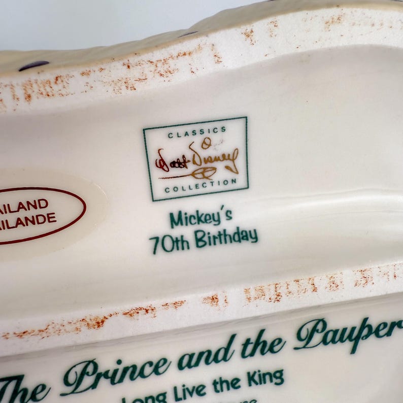 Op de afbeelding: Een wit keramisch verzamelobject met de tekst "Mickey's 70th Birthday" en "The Prince and the Pauper". Het heeft een "Walt Disney Collection" logo en is gemaakt in Thailand.