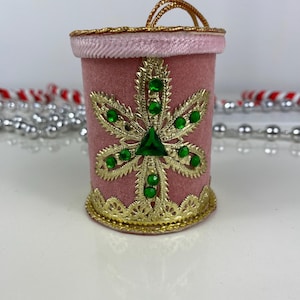 May include: A pink velvet Christmas ornament with a gold trim and a green jeweled snowflake design.
